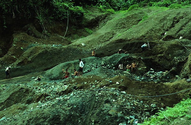 Heavily eroded dirt and stone slope with many semi-clad gold miners hacking away in channels