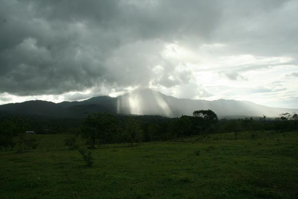 Volcan Cacao seen from the east with forest wrapping all around it, under heavy rain clouds